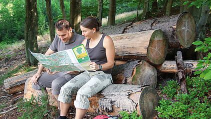 Wo geht's auf dem Drahthandelsweg weiter? Zwei Wanderer mit Wanderkarte sitzend auf einem Baumstumpf
